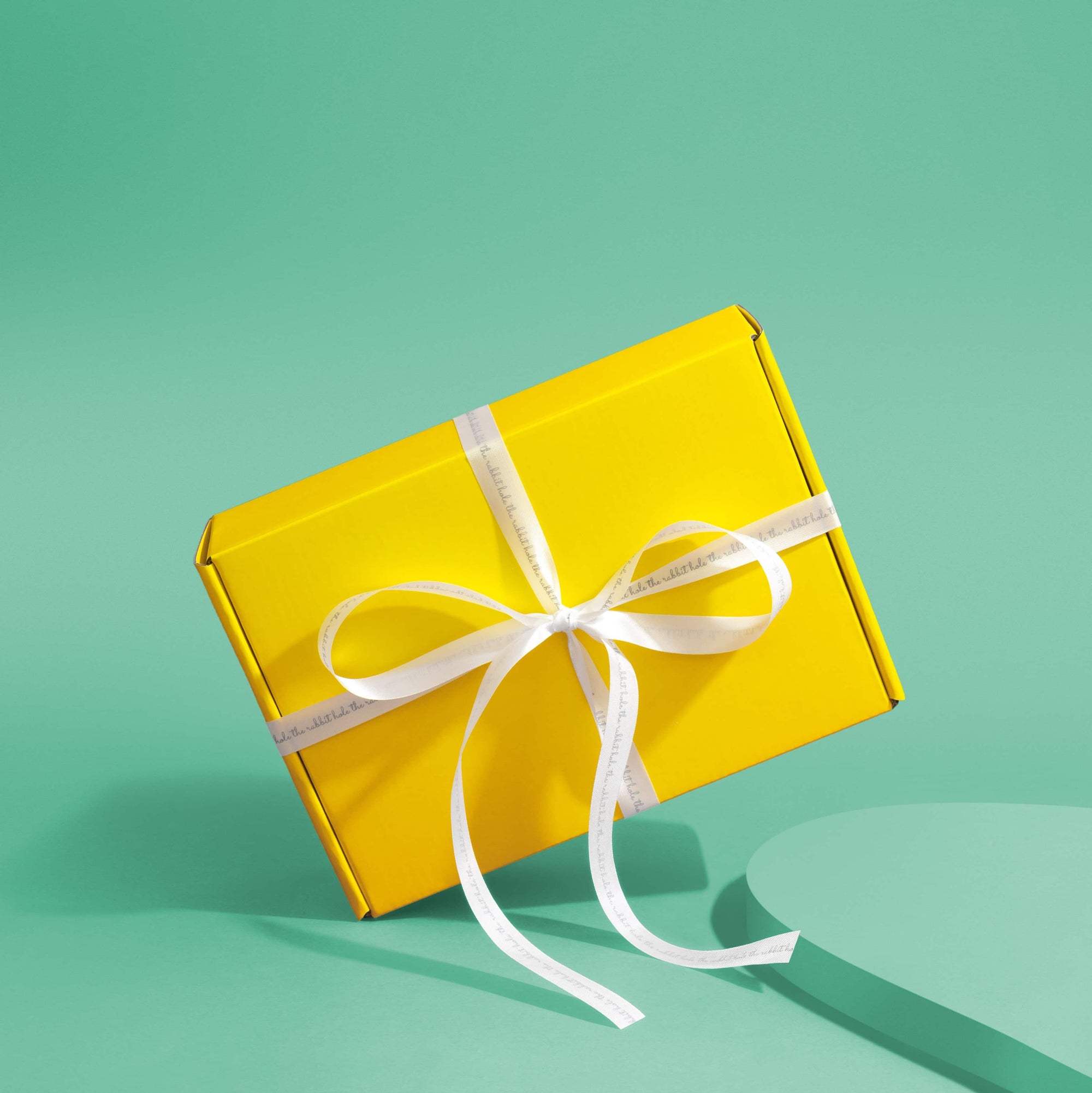 Yellow gift box with white ribbon on green background by The Rabbit Hole